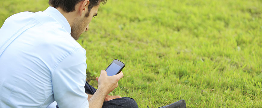male is using his phone while sitting on the grass